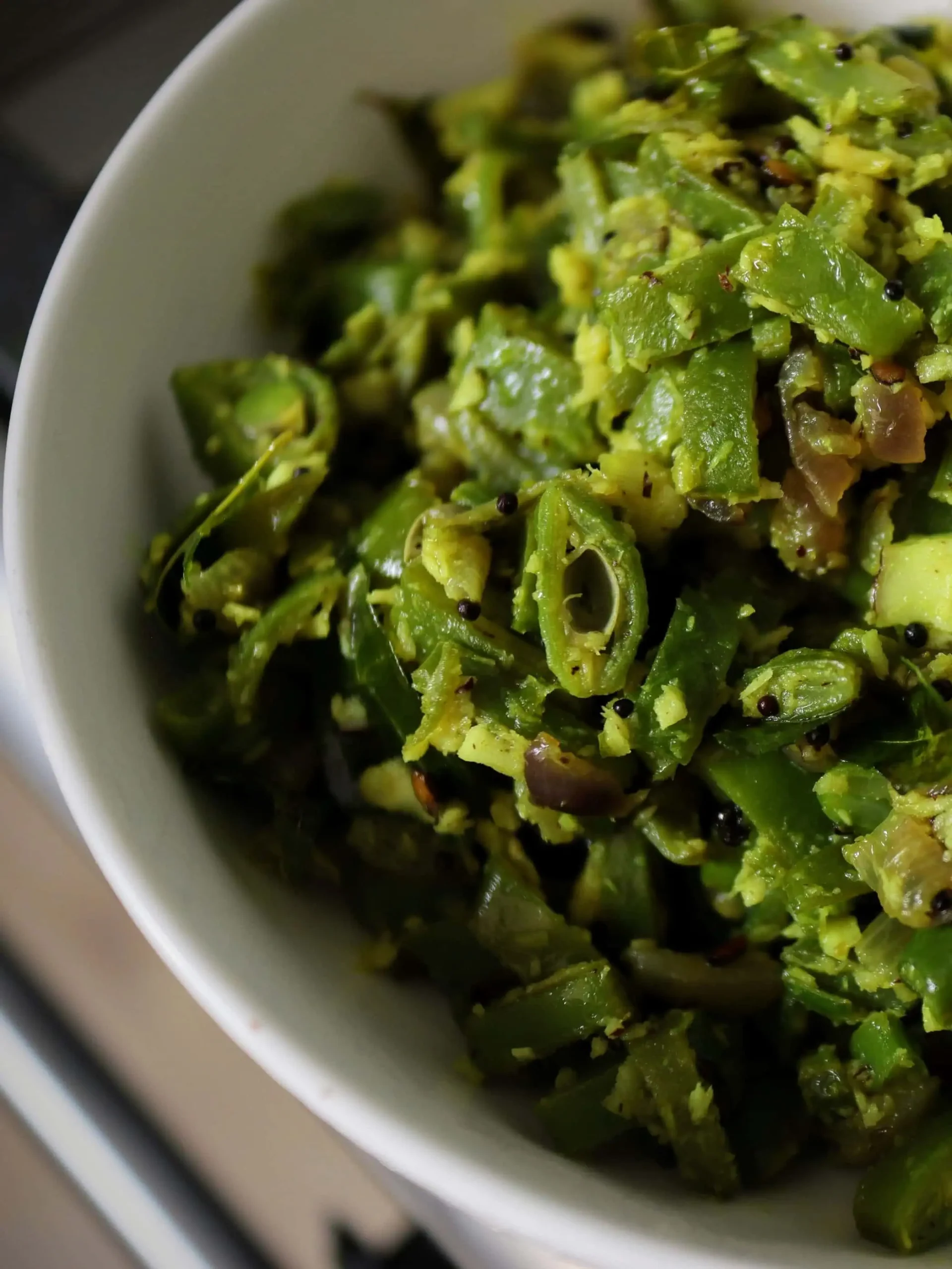 Vibrant green beans thoran served in a traditional Kerala-style bronze dish, garnished with fresh curry leaves and grated coconut, showcasing the authentic South Indian preparation