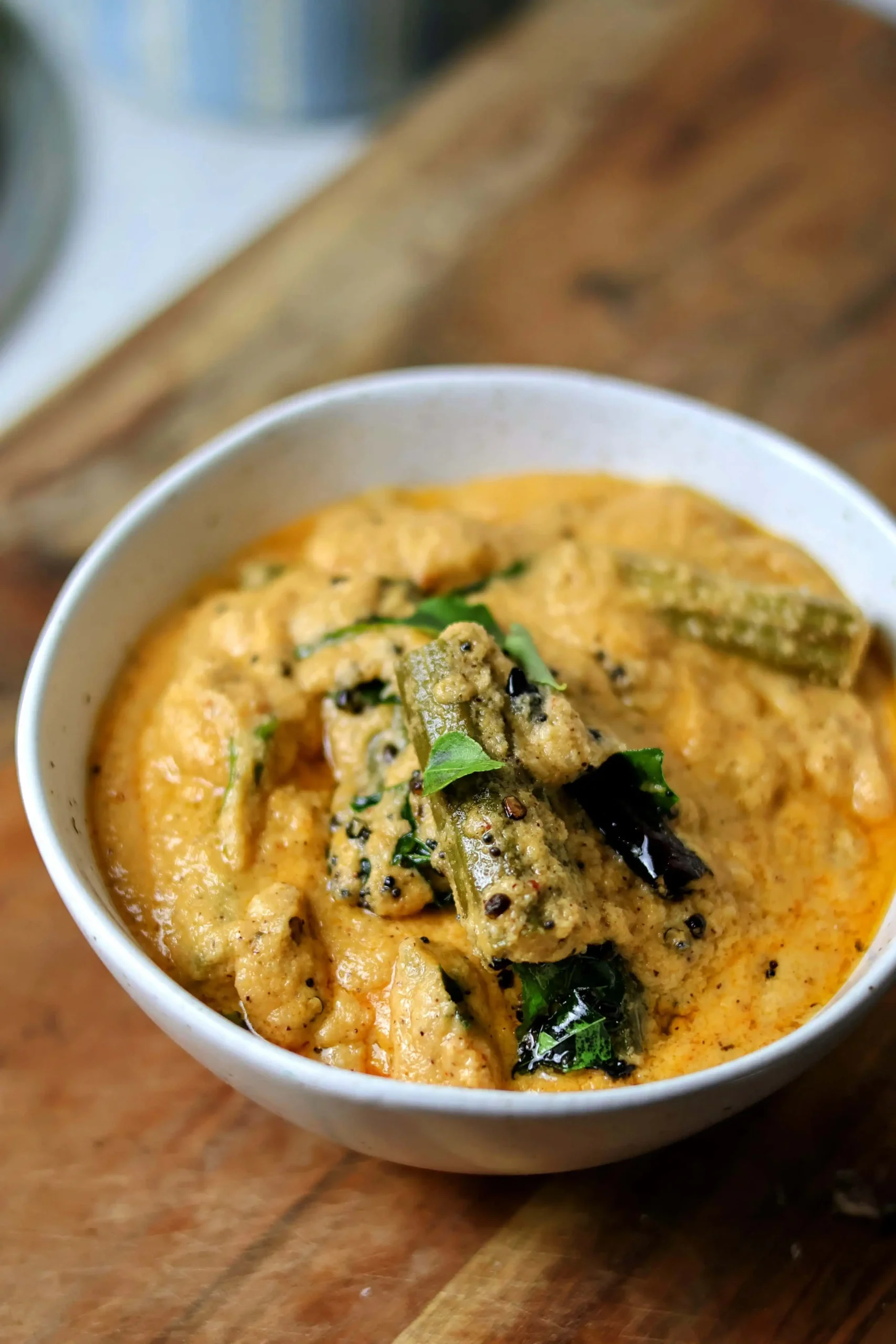 Drumsticks ava kura served in a traditional copper bowl, featuring tender moringa pods in a golden-brown curry gravy garnished with fresh curry leaves and coriander, served alongside steaming white rice