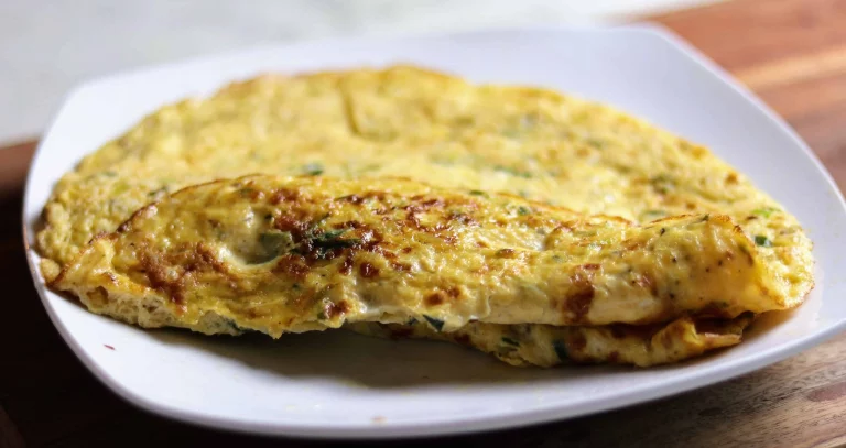 A freshly made, fluffy Indian omelette sits folded in half on a plate