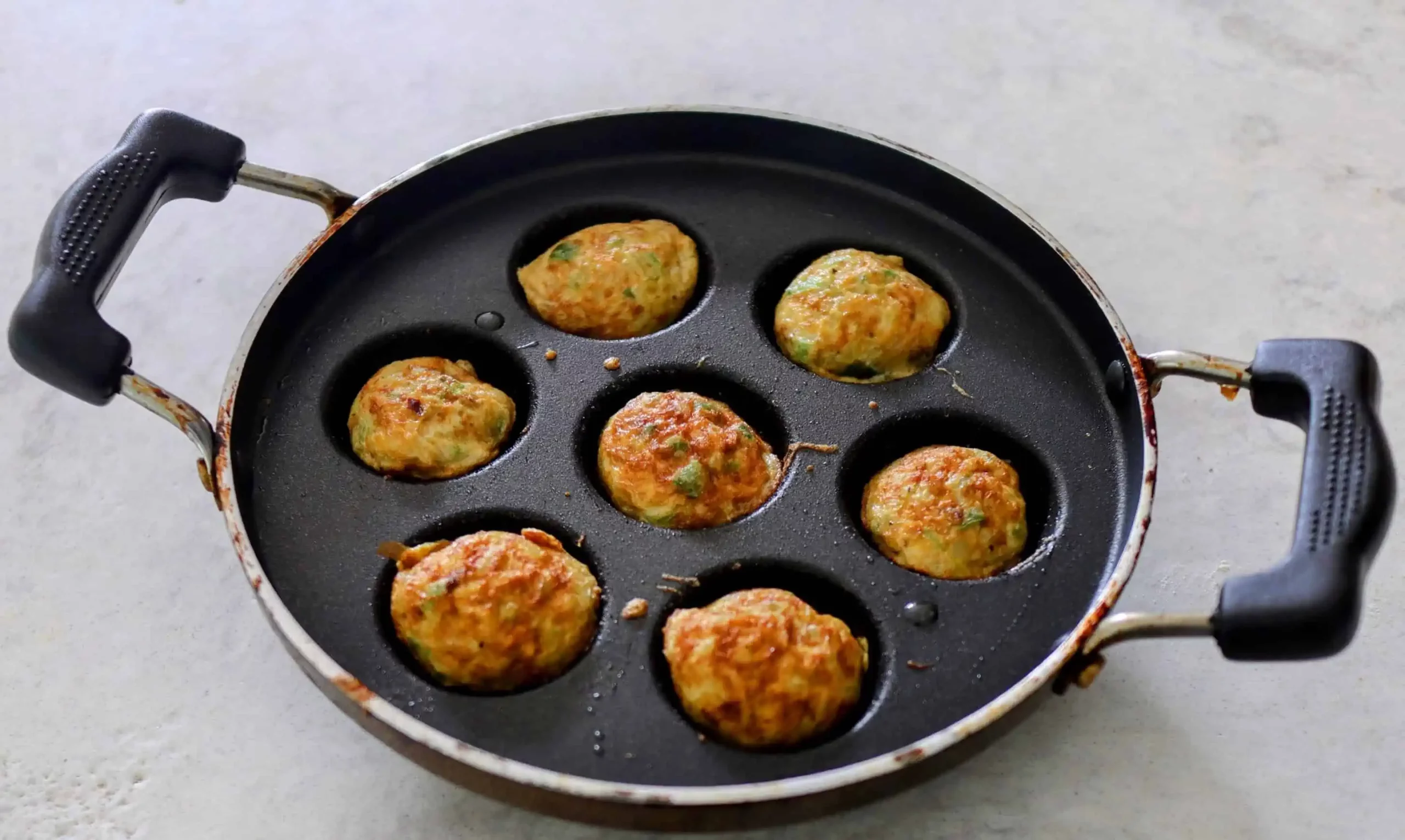 A paniyaram pan with seven small egg kuli paniyarams, also known as mutta paniyarams