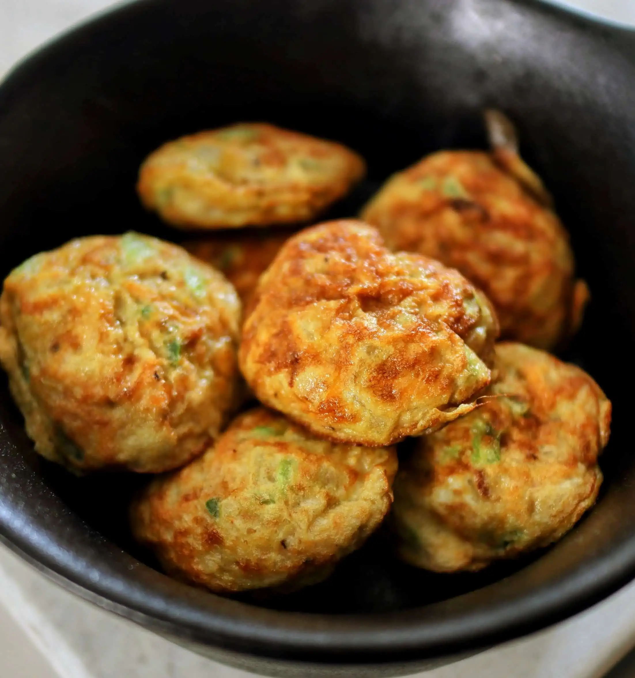 An appetizing sight of egg paniyaram, a fried food, served in a bowl on a kitchen counter.