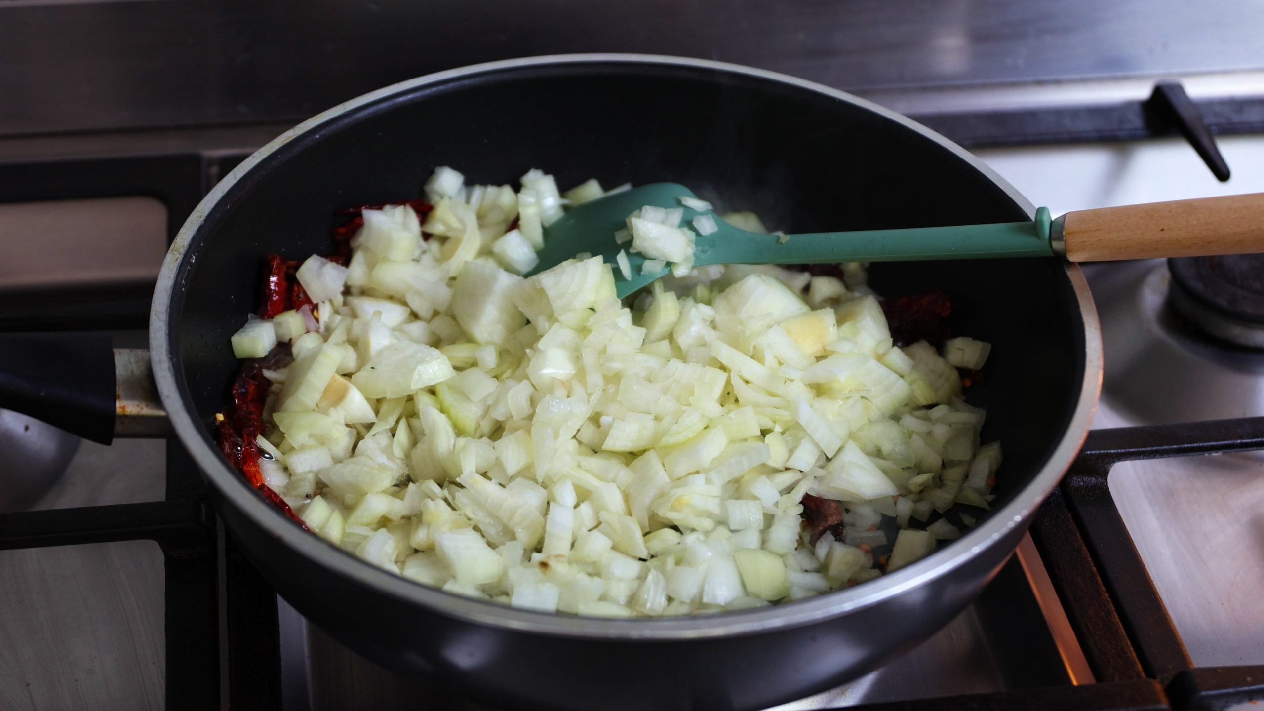 sauce pan with coconut oil and mustard seeds, urad dal, red chillies and onions added for making kale stir fry