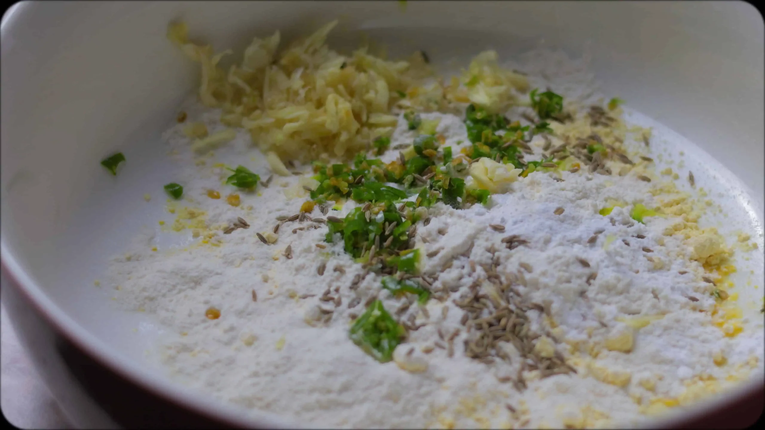 Bowl of zucchini fritter batter showing combined ingredients with visible herbs and spices