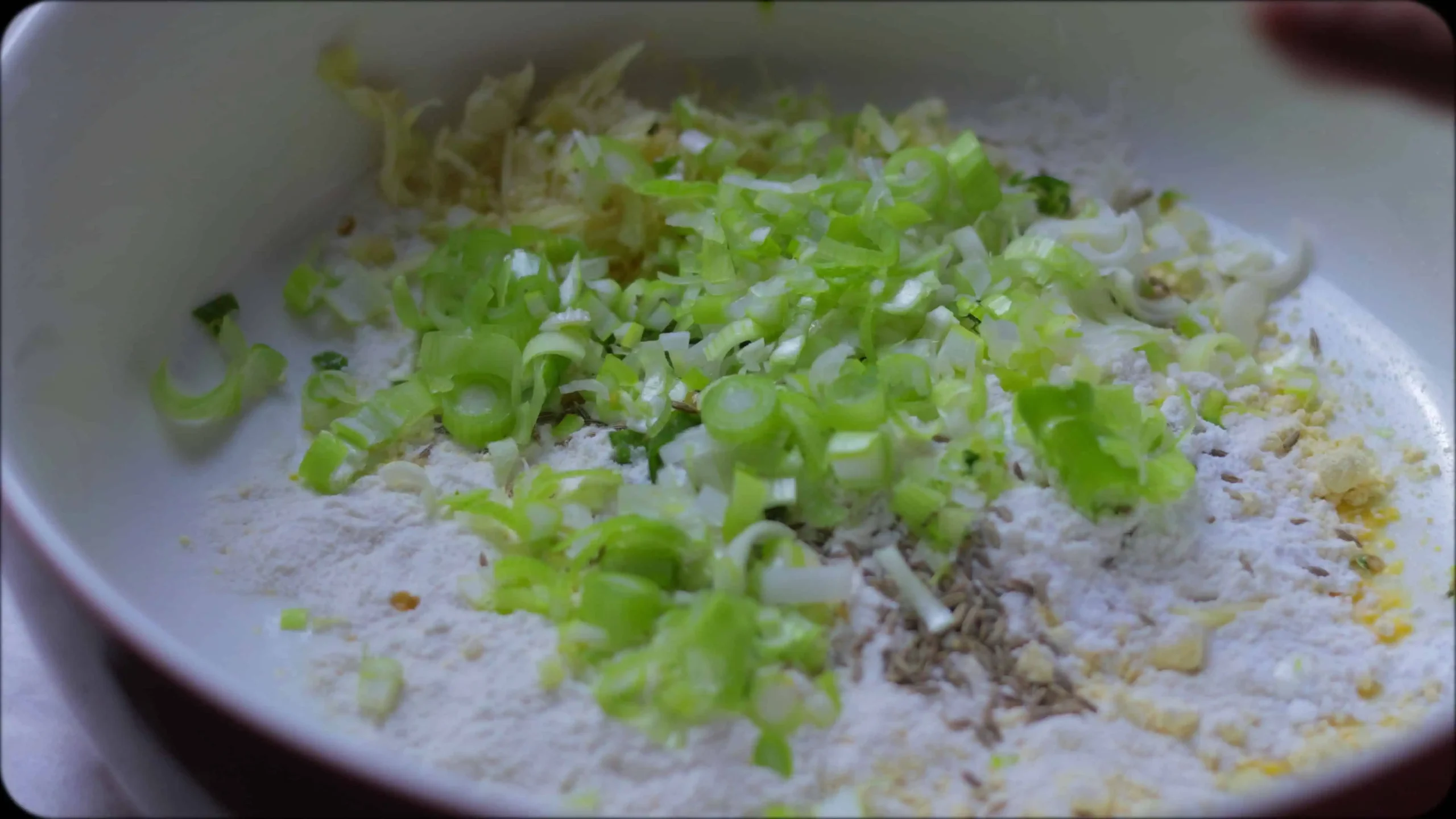 Bowl of zucchini fritter batter showing combined ingredients with visible herbs and spices