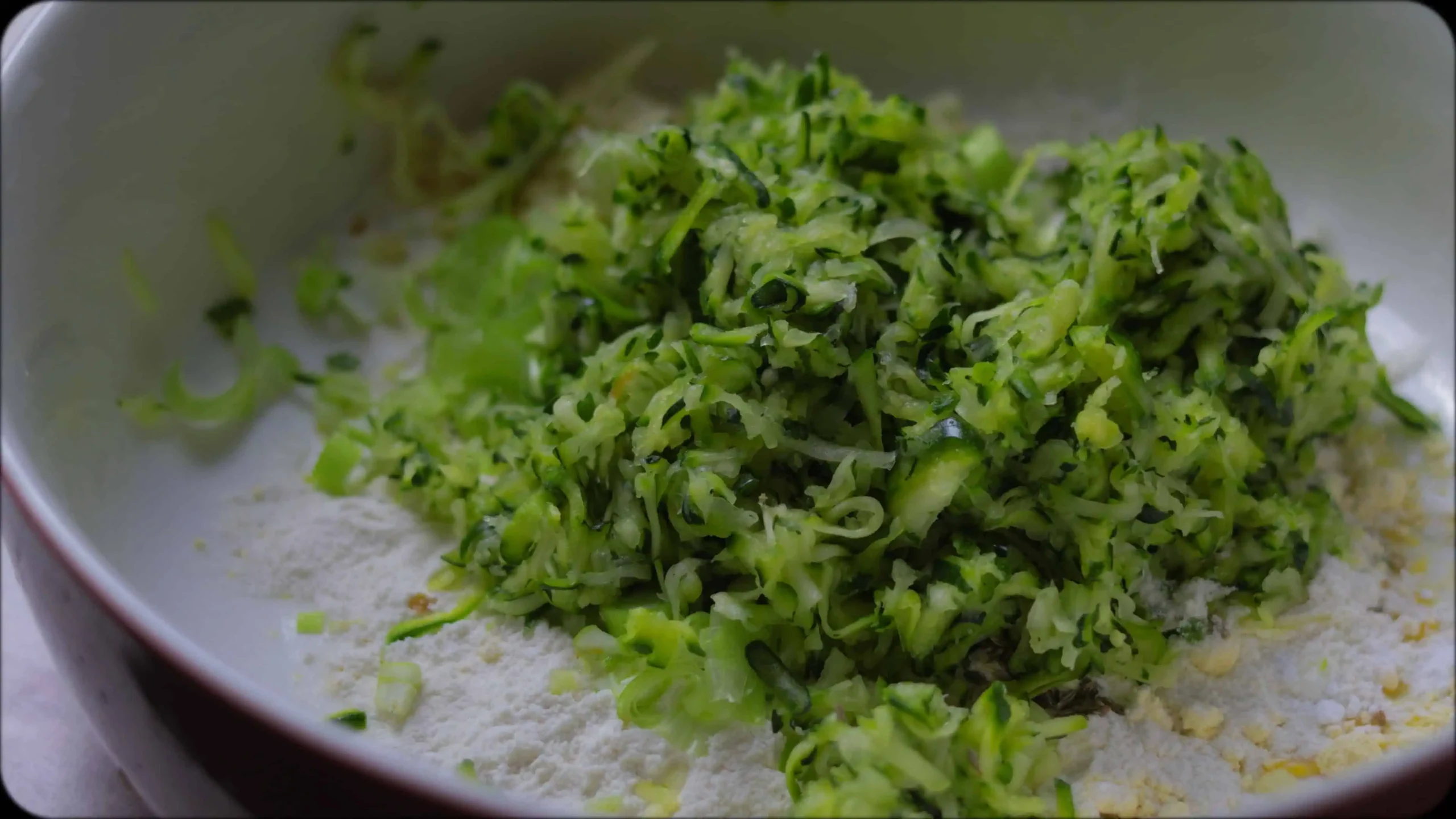 Bowl of zucchini fritter batter showing combined ingredients with visible herbs and spices